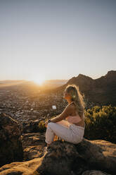 Frau sitzt bei Sonnenaufgang auf einem Felsen - LHPF01511