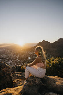 Woman sitting on rock at sunrise - LHPF01511