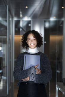 Lächelnde Geschäftsfrau mit Laptop im Korridor eines Büros - MCVF01051