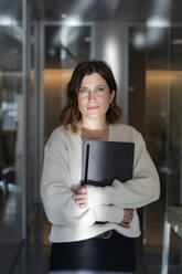 Geschäftsfrau mit Laptop im Korridor eines Büros - MCVF01053