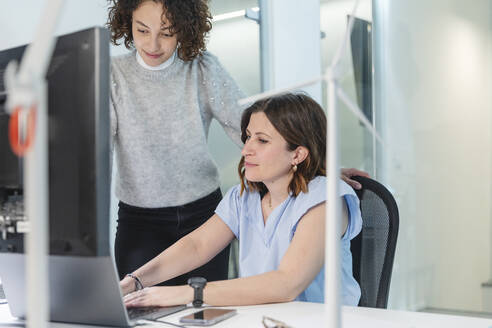 Geschäftsfrau diskutiert mit Kollege über Laptop am Schreibtisch im Büro - MCVF01055