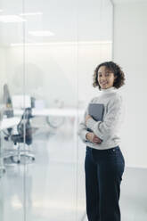 Selbstbewusste Geschäftsfrau mit Laptop an einer Glaswand im Büro - MCVF01058