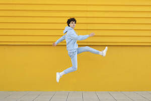 Unbekümmerter junger Mann, der vor einer gelben Wand springt - LMCF00124