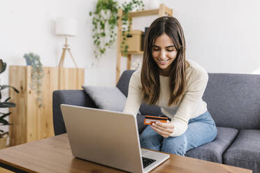 Happy woman with credit card doing online shopping on laptop at home - XLGF03234