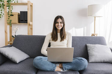 Lächelnde Frau mit Laptop im Schneidersitz zu Hause - XLGF03236