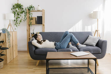 Woman lying down on sofa in living room - XLGF03244