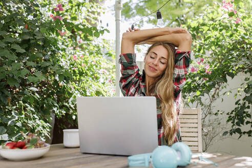 Freelancer stretching arms sitting with laptop at table - TYF00743