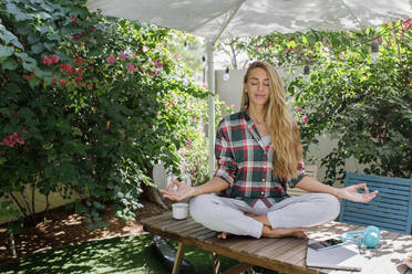 Freelancer practicing yoga sitting on table in back yard - TYF00745