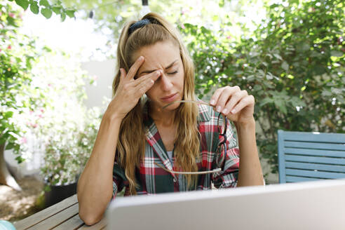 Tired freelancer rubbing eye at table in back yard - TYF00751