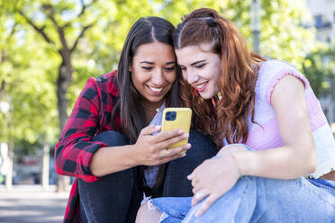 Woman sharing smart phone with girlfriend at footpath - WPEF07303