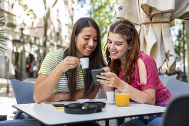 Glückliche Frau teilt ihr Smartphone mit ihrer Freundin in einem Straßencafé - WPEF07324