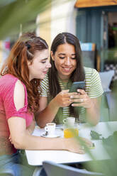 Woman sharing smart phone with girlfriend in sidewalk cafe - WPEF07325