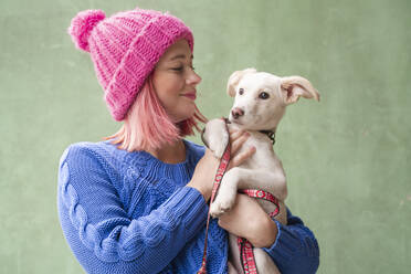 Smiling woman carrying cute puppy over green wall - OSF01392