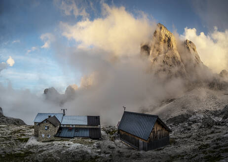 Häuser unter bewölktem Himmel vor dem Berg Cima del Focobon bei der Mulaz-Hütte, Dolomiten, Italien - ALRF02070