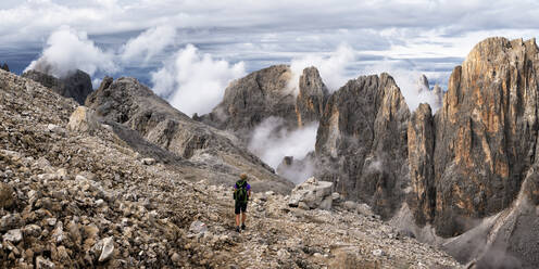 Senior woman hiking on mountain under cloudy sky at Pala di San Martino, Dolomites, Italy - ALRF02082