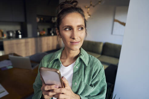 Thoughtful woman with mobile phone at home office - ABIF01828