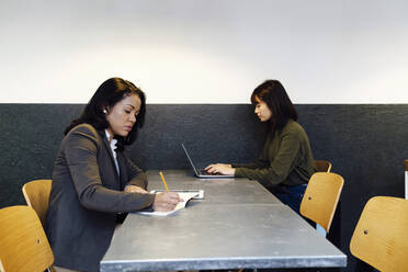 Geschäftsfrauen, die zusammen an einem Schreibtisch im Büro sitzen - ASGF03298