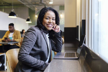Lächelnde Geschäftsfrau mit Laptop auf dem Tisch am Arbeitsplatz - ASGF03309