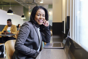 Smiling businesswoman with laptop on table at workplace - ASGF03309