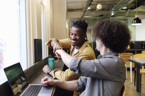 Smiling business colleagues giving fist bump at workplace - ASGF03327