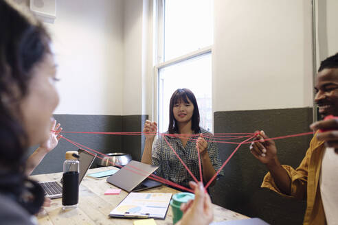 Multiracial business colleagues playing cat's cradle in break time at workplace - ASGF03340