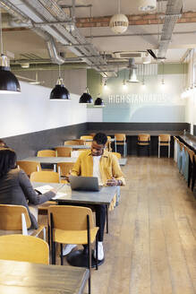 Geschäftsmann bei der Arbeit mit einem Kollegen, der am Tisch in der Büro-Cafeteria sitzt - ASGF03382