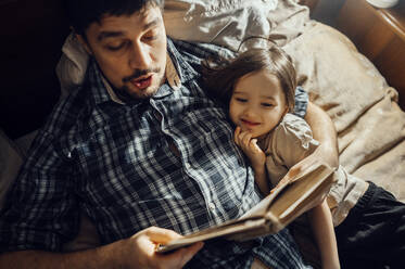 Father reading story book lying with son on bed - ANAF00996