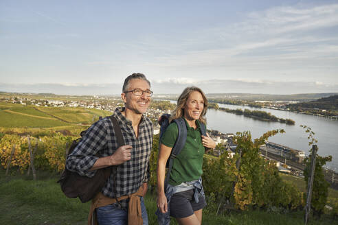 Glückliches reifes Paar beim Wandern durch Weinberge unter blauem Himmel - RORF03361