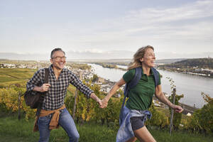 Glückliches Paar hält sich an den Händen und genießt das Wandern auf einem Hügel - RORF03362