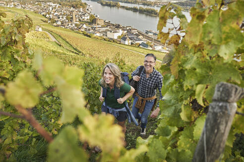 Lächelnder reifer Mann und Frau wandern auf einem Hügel mit einer Stadt im Hintergrund - RORF03369