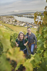 Glücklicher reifer Mann mit Frau beim Wandern auf einem Hügel in einem Weinberg - RORF03372