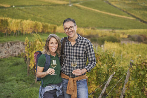 Glückliche Touristen mit Weingläsern in einem Weinberg stehend - RORF03383