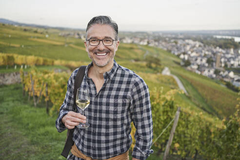 Glücklicher reifer Mann mit Weinglas auf einem Hügel - RORF03389