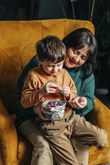 Glückliche Großmutter mit Enkel, der einen Korb mit Schokoladeneiern zu Ostern hält - VSNF00448