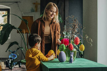Lächelnde Mutter und Sohn dekorieren den Tisch für das Osteressen zu Hause - VSNF00456