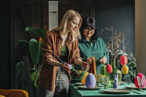 Happy woman with mother setting table for Easter dinner at home - VSNF00461