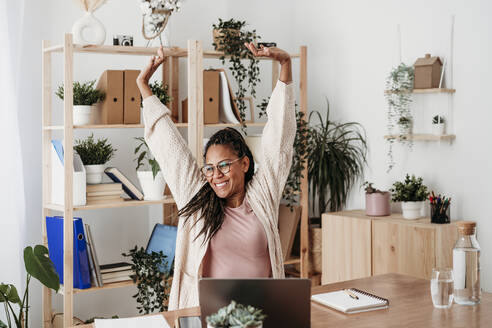 Smiling mature freelancer stretching arms at desk - EBBF07963