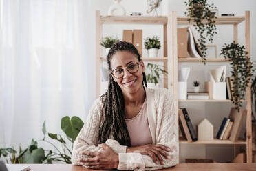 Smiling freelancer wearing eyeglasses sitting at desk - EBBF07998