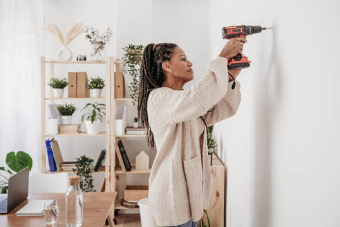 Frau mit Bohrmaschine an der Wand zu Hause - EBBF08013