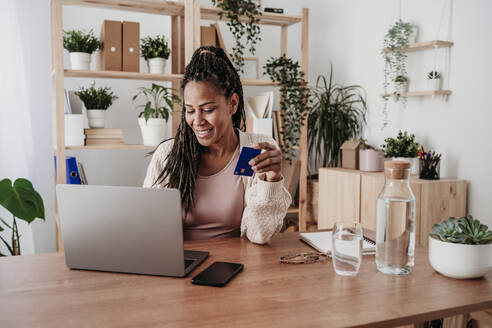 Smiling freelancer paying with credit card on laptop at home office - EBBF08015