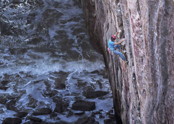 Man climbing rocky mountain by sea - ALRF02087