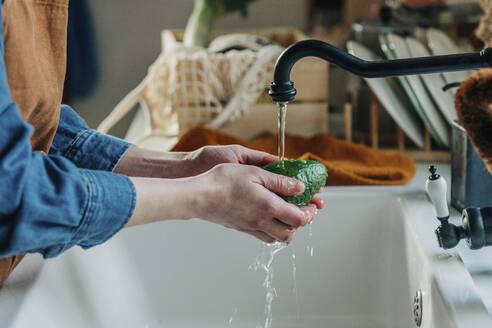 Hands of woman washing avocado in kitchen sink - VSNF00481