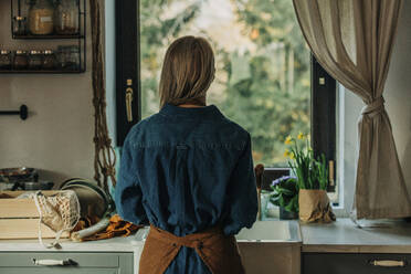 Frau steht in der Küche und schaut aus dem Fenster - VSNF00482