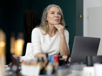 Businesswoman sitting with hand on chin at workplace - FLLF00856