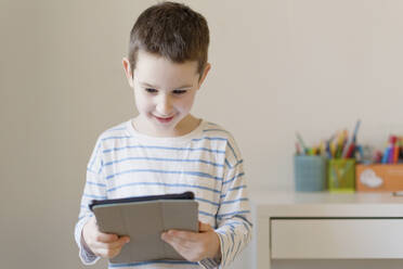 Smiling boy watching tablet PC at home - ONAF00415