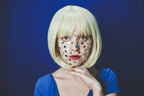 Blond woman with small mirrors on face against blue background - SVCF00311