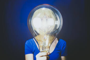 Woman holding large illuminated bulb against blue background - SVCF00316