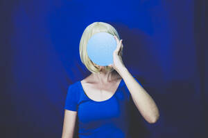 Frau bedeckt Gesicht mit blauem Kreis vor farbigem Hintergrund - SVCF00318