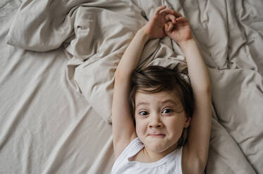 Playful boy stretching on bed at home - ANAF01000