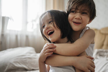 Glücklicher Junge umarmt Bruder im Schlafzimmer zu Hause - ANAF01002